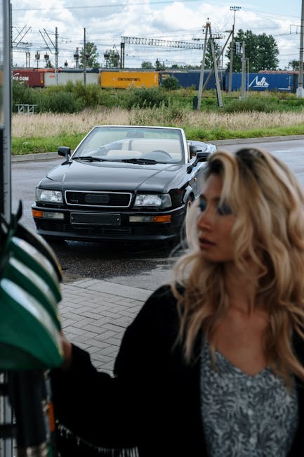 Blonde woman refueling her convertible at an outdoor gas station.