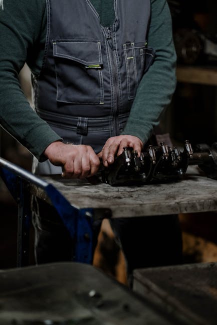 Close-up of a male mechanic disassembling a car engine in a dimly lit workshop.